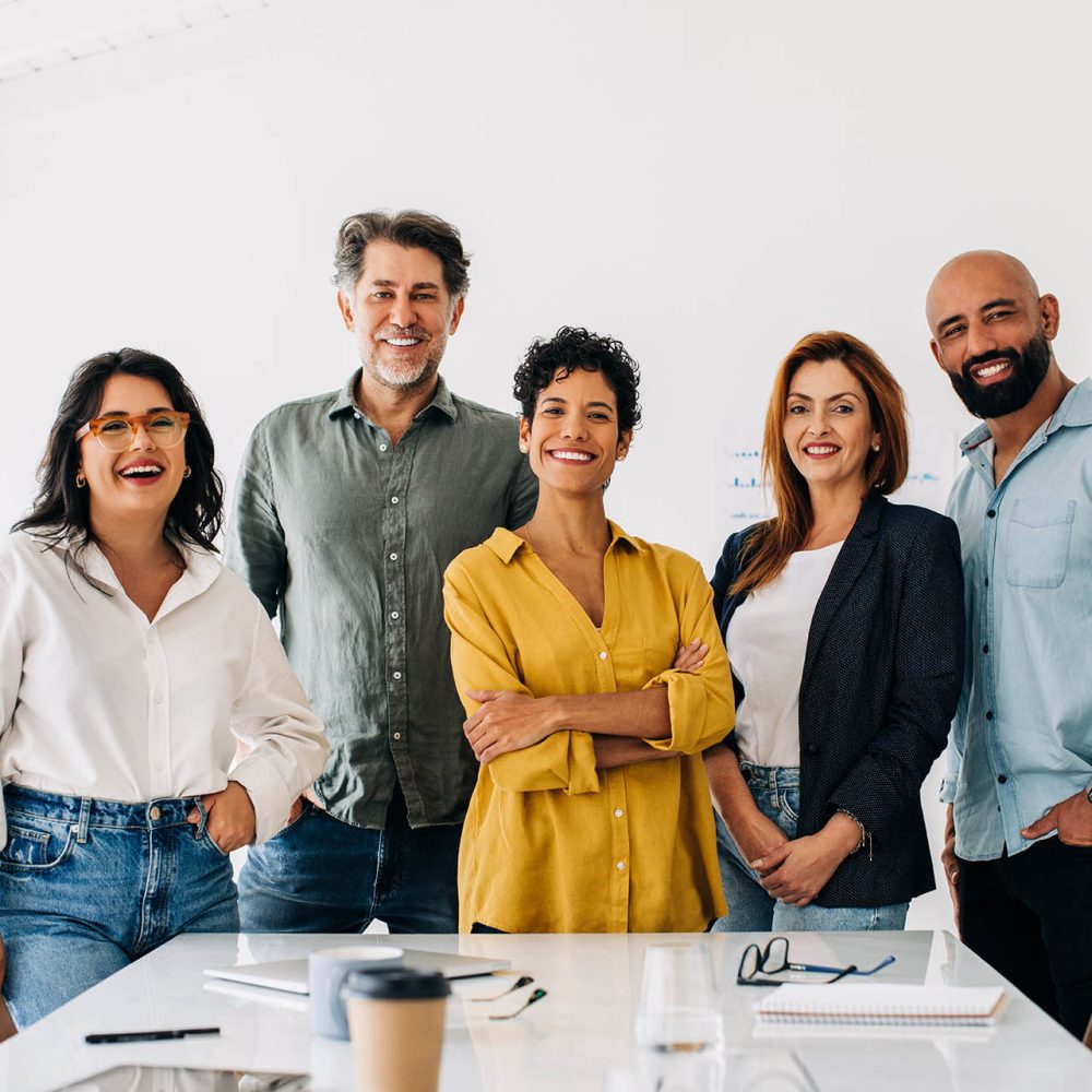 Successful business team standing together in a boardroom. Group of diverse business professionals smiling at the camera. Creative business people having a meeting in an office.